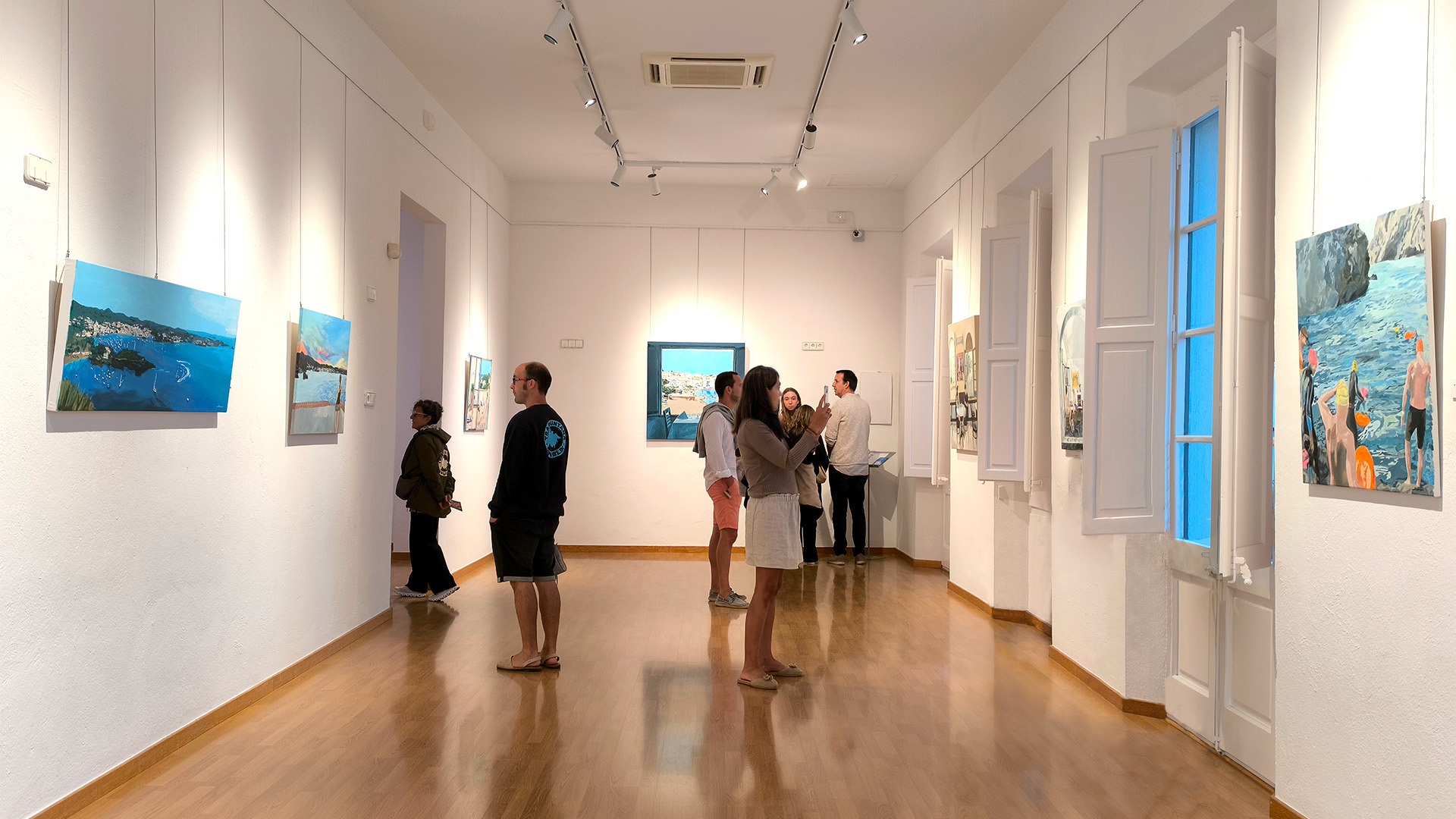 Visitants observant les obres de l’exposició “Moments” de Marta Serra Pou a la sala gran de la mostra.