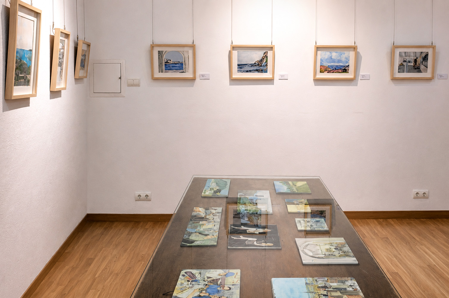 Vista de la sala petita de l’exposició “Moments”, amb obres de petit format a les parets i una taula de vidre amb llibretes d’esbossos com a inici del recorregut expositiu.
